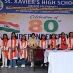 Group of students in white outfits with orange scarves standing on a stage during an independence day celebration at st Xaviers high school india